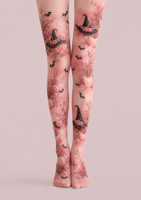 A pair of sheer pink tights with a Halloween-themed print featuring black witch hats, bats, and pumpkins, shown on a model's legs against a solid pale pink background.