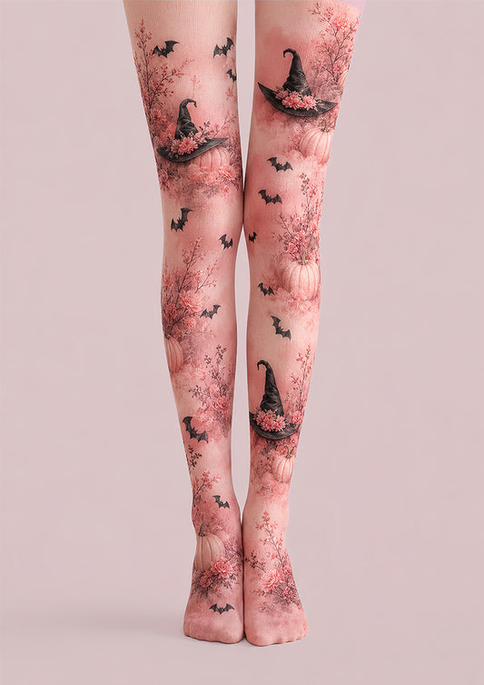 A pair of sheer pink tights with a Halloween-themed print featuring black witch hats, bats, and pumpkins, shown on a model's legs against a solid pale pink background.
